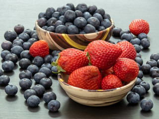 Blueberries and Strawberries in ceramic bowls and on a black wooden table. Healthy red berry snack. Fresh vegan breakfast. Close up. Bunch of vitamins.
