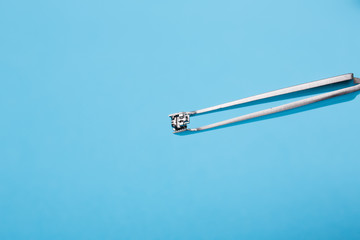 Macro shooting. Orthodontist holds a brace with tweezers on a blue background