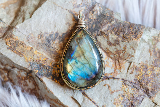 Brass pendant with natural labradorite gemstone on rocky background