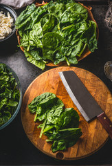 Fresh spinach on wooden cutting board with knife on dark rustic table background. Top view. Home...