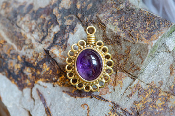 Brass pendant with natural ametyste gemstone on rocky background - 347720998