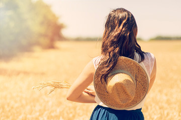 concept - a beautiful young woman with a hat walking in a field of wheat. the view from the back