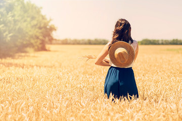 concept - a beautiful young woman with a hat walking in a field of wheat. the view from the back