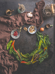 Food background with fresh colorful chard leaves on dark rustic table  background with herbs and spices. Top view. Circle frame. Country style. Clean organic food. Paleo dieting. Home cuisine.