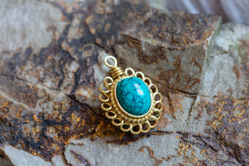 Brass pendant with natural turquoise gemstone on rocky background