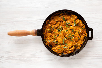 Homemade Chicken Tikka Masala in a cast iron pan on a white wooden table, top view. Flat lay, overhead, from above.