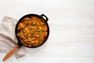 Homemade Chicken Tikka Masala in a cast iron pan on a white wooden table, top view. Flat lay, overhead, from above. Space for text.