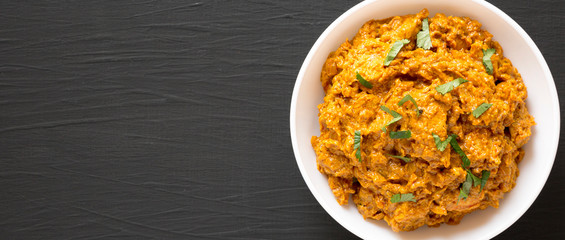 Homemade Chicken Tikka Masala in a white bowl on a black surface, top view. Flat lay, overhead, from above. Copy space.