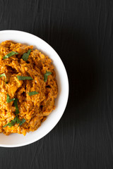 Homemade Chicken Tikka Masala in a white bowl on a black surface, top view. Flat lay, overhead, from above. Copy space.