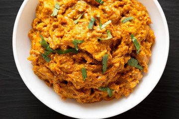 Homemade Chicken Tikka Masala in a white bowl on a black surface, top view. Flat lay, overhead, from above. Close-up.
