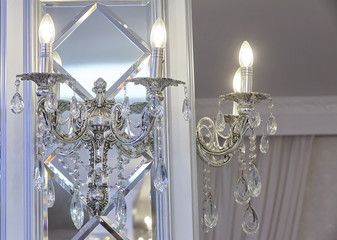 Two wall chandeliers in the form of candles on the mirror surface.