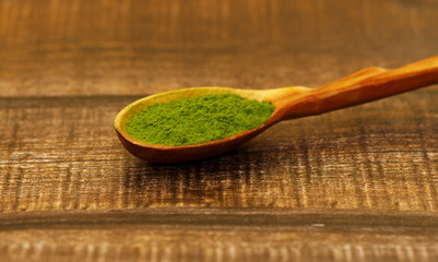 Green tea matcha in a spoon on a brown wooden background close-up. Matcha in a wooden spoon.