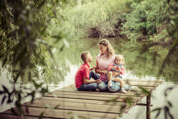Mom with son and daughter. family of mother, daughter and son is sitting on a wooden bridge near the river. Family picnic. mother with children. Happy family on a walk