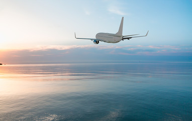 Airplane flying above tropical sea at sunset