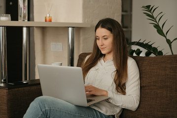 Fototapeta premium Remote work. A caucasian woman working remotely on her laptop. A businesswoman working from home on the sofa.