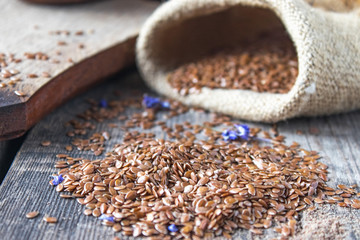 Flax seeds on a wooden background near a bag with seeds.