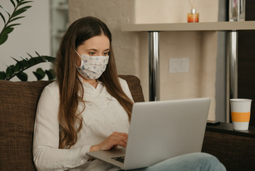 Remote work. A woman in a medical face mask working remotely on her laptop during the quarantine to...