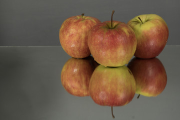 Fototapeta na wymiar Three red apples on mirroring table on mirror gray background with reflection isolated close up