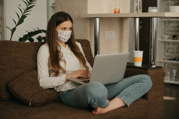 Remote work. Woman in a medical face mask studying remotely on her laptop during the quarantine to avoid the spread coronavirus. A girl working from home in a face mask during the pandemic of COVID-19