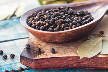 Black pepper in a spoon lies on a cutting board near the bay leaf on a background of blue boards.
