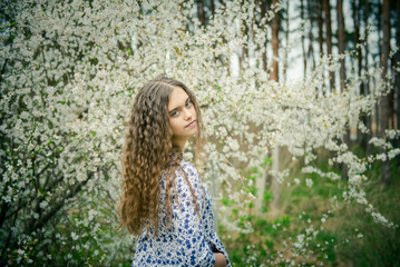 Fototapeta na wymiar Beautiful Girl with long hair in the spring. Girl teenager in the spring among the blooming garden. Happy girl in a blooming apricot garden. beautiful girl with wavy hair. Long hair