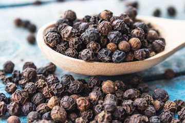 Dry black pepper in a wooden spoon near black pepper scattered on blue boards.