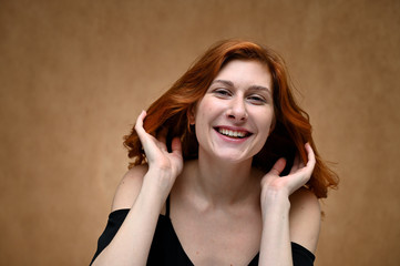 Studio large photo portrait of Caucasian young actress woman with long red hair on a beige background. Model poses with a smile and grimace.