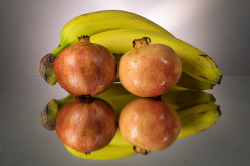 Yellow bananas and red pomegranate on mirroring table. Gorizontal image
