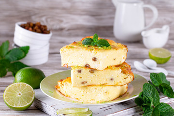 Cottage cheese casserole with raisins and mint, lime slices on a plate on a wooden table