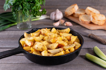 Fried potatoes in a rural style, with spices and fresh greens. On rustic pan, on a wooden table.