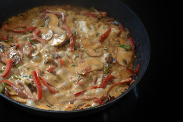 Creamy vegetable ragout with bell pepper, mushroom and onion in a pan on a black stove, copy space