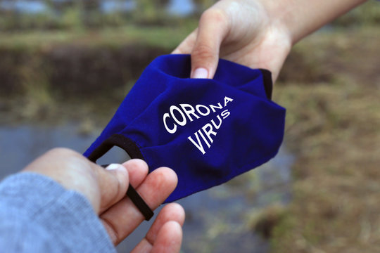 Hands holding face mask with text sign on it - Corona Virus. To prevent pandemic corona virus COVID-19 concept with blue cloth face mask in young man woman hands. 
