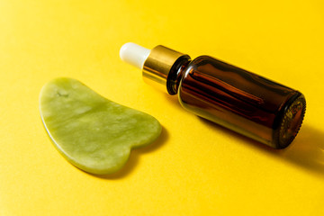 Glass bottle with pipette and jade gua sha at yellow background