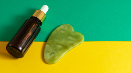 Gua sha tool with glass bottle serum at yellow backgorund. Massage with gua sha concept. Selective focus