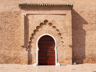 Naklejka na ściany i meble Wooden door of the Kutubiyya Mosque, Marrakesh, Morocco. Moroccan closed archway gate in stone terracotta wall with islamic ornaments
