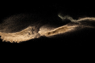 Plakat Brown sand explosion isolated on black background. Freeze motion of sandy dust splash.Sand texture concept.