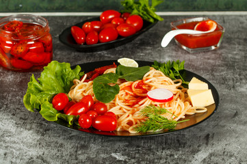 Spaghetti with tomato sauce, cherry tomatoes and basil on a dark background. Tasty appetizing classic italian spaghetti pasta with tomato sauce, cheese parmesan and basil on plate on dark table. 