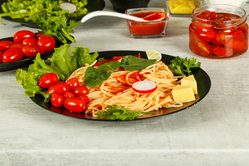 Spaghetti with tomato sauce, cherry tomatoes and basil on a dark background. Tasty appetizing classic italian spaghetti pasta with tomato sauce, cheese parmesan and basil on plate on dark table. 