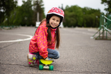 Cute little preteen girl wearing helmet riding on a skateboard in beautiful summer park