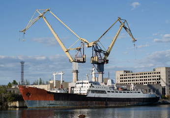 Fototapeta premium The ship is in port. Ship at the pier. Merchant ship. Rusty metal. Cargo crane.