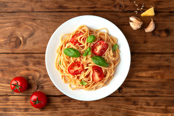 Spaghetti in tomato sauce with cheese and basil on a wooden background