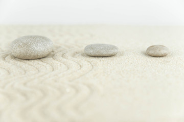 Fototapeta na wymiar Zen garden. Pyramids of white and gray zen stones on the white sand with abstract wave drawings. Concept of harmony, balance and meditation, spa, massage, relax.