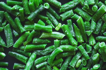 On a black background lies a frozen green ripe string bean, used as an ingredient in the dish.