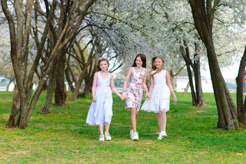 Naklejka na ściany i meble Three adorable girls in dresses hold hands in the garden, park.
