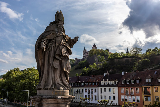 Würzburg, Germany - 10th May 2020: A german photographer visiting the city center, taking pictures of religious statues on the footbridge called old Maria bridge at a cloudy day in spring.