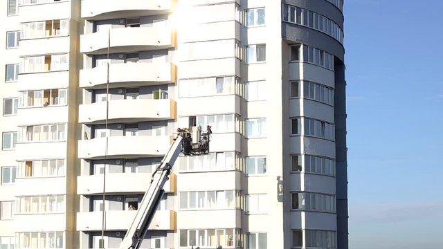 Aerial platform fire truck raises firefighters in a protective basket to extinguish a fire in a multi-story high-rise building, fireman