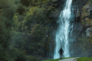 A man stands with amazement as he watches a powerful canyon waterfall of the Italian Alps. 