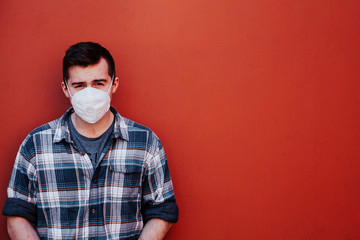 a guy in a checked shirt and mask on a red background looks at the camera standing on the left side of the frame