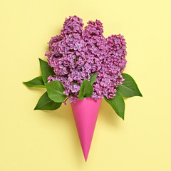 Lilac blossom spring bouquet in ice cream cone. Pink bloom flowering, top view. Minimal creative concept. Springtime lilac blooming. Trendy yellow vivid fashionable design.