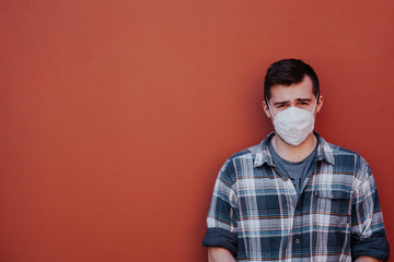 a guy in a checked shirt and mask on a red background looks at the camera. standing to the right of the frame